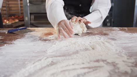 Asian-female-baker-working-in-bakery-kitchen,-kneading-dough-on-counter-in-slow-motion