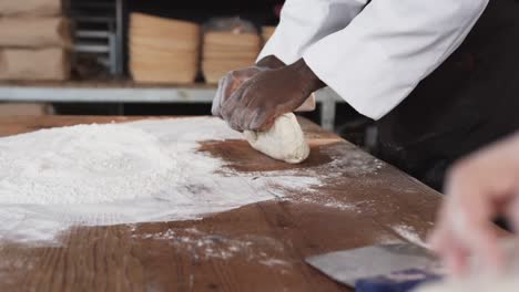 Diverse-bakers-working-in-bakery-kitchen,-kneading-dough-on-counter-in-slow-motion
