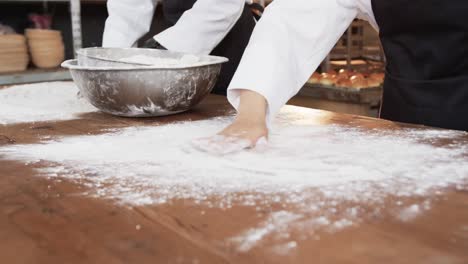 Diverse-bakers-working-in-bakery-kitchen,-spreading-flour-on-counter-in-slow-motion