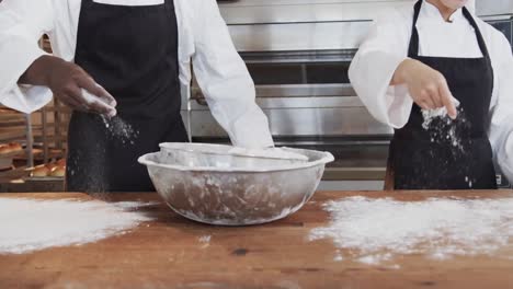 Diverse-bakers-working-in-bakery-kitchen,-pouring-flour-on-counter-in-slow-motion