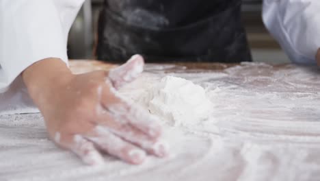 Asian-female-baker-working-in-bakery-kitchen,-gathering-flour-on-counter-in-slow-motion