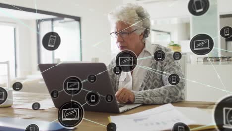 Animation-of-network-of-connections-with-icons-over-african-american-senior-woman-using-laptop