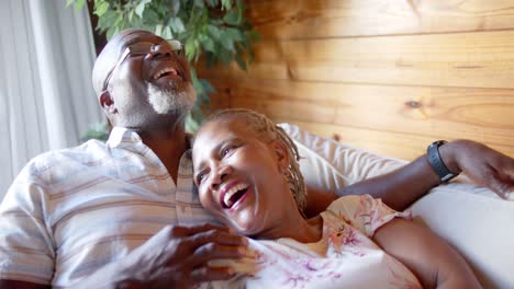 Happy-senior-african-american-couple-lying-on-sofa-at-home,-slow-motion
