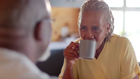 Happy-senior-african-american-couple-drinking-coffee-and-talking-in-kitchen,-slow-motion
