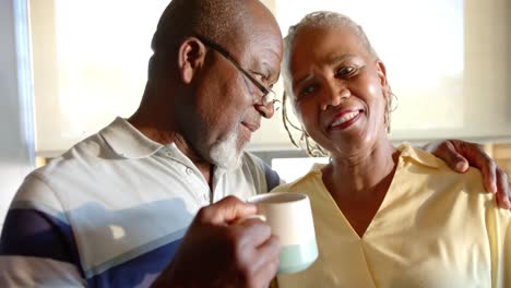 Happy-senior-african-american-couple-drinking-coffee-and-embracing-in-kitchen,-slow-motion