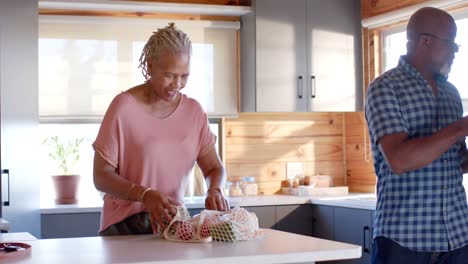 Happy-senior-african-american-couple-unpacking-groceries-in-kitchen,-slow-motion