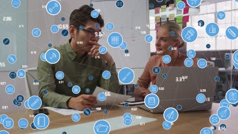 Animation-of-network-of-digital-icons-over-diverse-man-and-woman-discussing-at-office