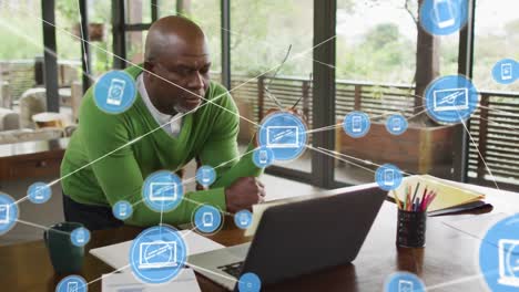 Animation-of-network-of-digital-icons-over-focused-african-american-man-looking-at-laptop-at-office