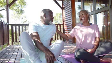 Glückliches-älteres-Afroamerikanisches-Paar,-Das-Auf-Matten-Sitzt-Und-Auf-Der-Sonnigen-Terrasse-Redet,-Zeitlupe