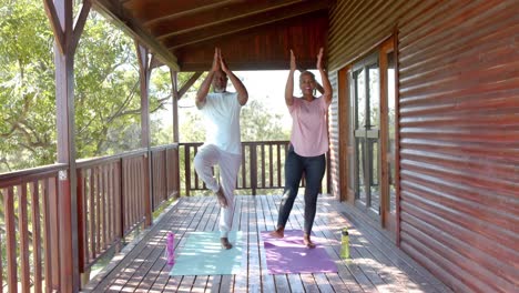 Glückliches-älteres-Afroamerikanisches-Paar,-Das-Yoga-Auf-Matten-Auf-Der-Sonnigen-Terrasse-Praktiziert,-Zeitlupe