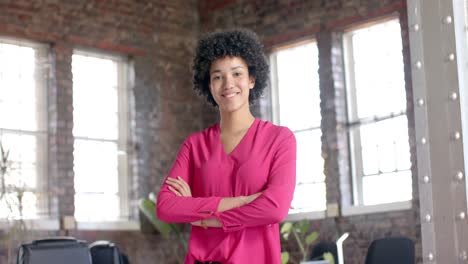 Portrait-of-happy-biracial-casual-businesswoman-with-arms-crossed-in-office-in-slow-motion