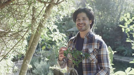Portrait-of-happy-caucasian-man-holding-plant-in-sunny-garden-with-copy-space,-slow-motion