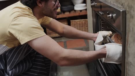 Happy-caucasian-man-pulling-bread-out-from-oven-in-kitchen,-slow-motion
