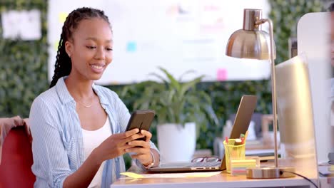 Happy-african-american-casual-businesswoman-using-laptop-and-smartphone-in-office,-slow-motion