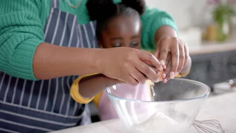 Midsection-of-african-american-mother-and-daughter-adding-egg-to-bowl-in-kitchen,-slow-motion