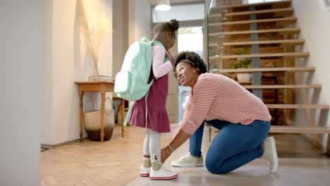 Happy-african-american-mother-advising-and-tying-shoes-of-daughter-at-home,-slow-motion