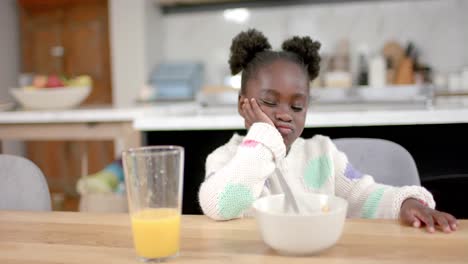 African-american-girl-eating-cereal-with-milk-in-kitchen,-slow-motion