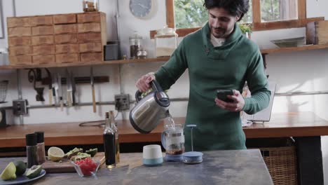 Kaukasischer-Mann-Kocht-Kaffee-Und-Benutzt-Smartphone-In-Der-Küche,-Zeitlupe