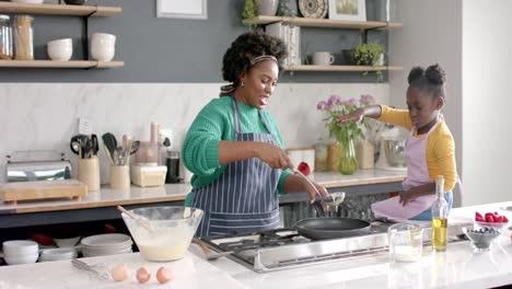Happy-african-american-mother-and-daughter-frying-pancakes-in-kitchen,-slow-motion