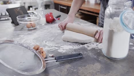 Hands-of-caucasian-man-preparing-bread-dough-using-tablet-in-kitchen,-slow-motion