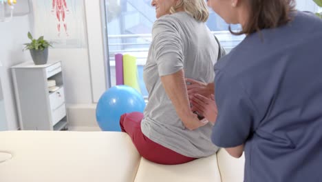 Fisioterapeuta-Femenina-Caucásica-Masajeando-La-Parte-Inferior-De-La-Espalda-De-Una-Paciente-Mayor-En-El-Centro-De-Rehabilitación