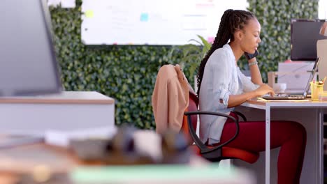 Afroamerikanische-Gelegenheitsgeschäftsfrau,-Die-Im-Büro-Einen-Laptop-Benutzt-Und-Auf-Dem-Smartphone-Spricht,-Zeitlupe