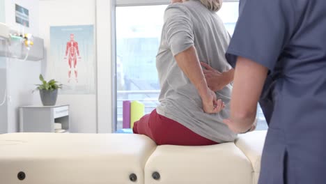 Caucasian-female-physiotherapist-massaging-lower-back-of-female-senior-patient-at-rehab-center