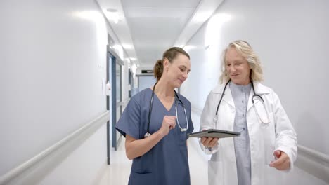 Caucasian-female-doctors-in-discussion-using-tablet-in-hospital-corridor,-slow-motion