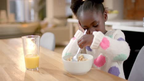 African-american-girl-eating-cereal-with-milk-in-kitchen,-slow-motion