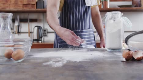 Midsection-of-caucasian-man-preparing-bread-dough-in-kitchen,-slow-motion