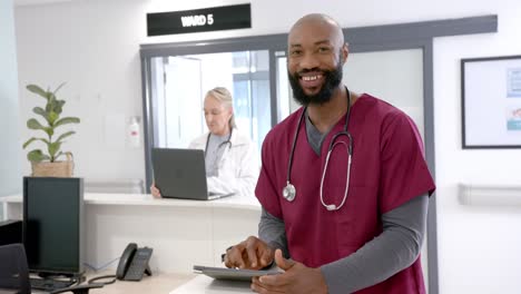 Porträt-Eines-Glücklichen-Afroamerikanischen-Männlichen-Arztes,-Der-An-Der-Krankenhausrezeption-Ein-Tablet-Verwendet,-Zeitlupe