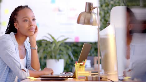 Thoughtful-african-american-casual-businesswoman-sitting-at-desk-with-laptop-in-office,-slow-motion