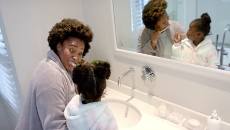 Happy-african-american-mother-and-daughter-brushing-teeth-in-bathroom,-slow-motion