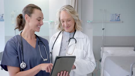 Happy-caucasian-female-doctors-in-discussion-using-tablet-in-hospital-room,-slow-motion