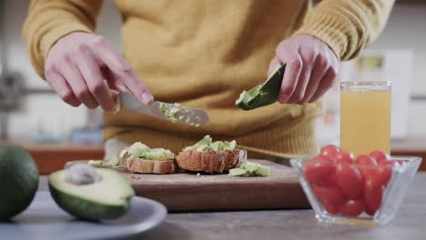 Midsection-of-caucasian-man-preparing-avocado-toast-in-kitchen,-slow-motion