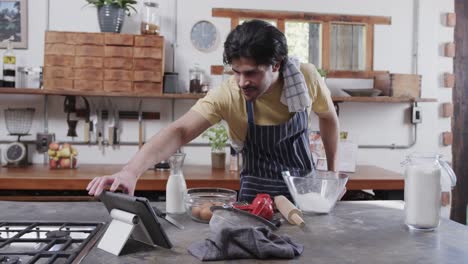 Hombre-Caucásico-Preparando-Masa-De-Pan-Usando-Tableta-En-La-Cocina,-Cámara-Lenta