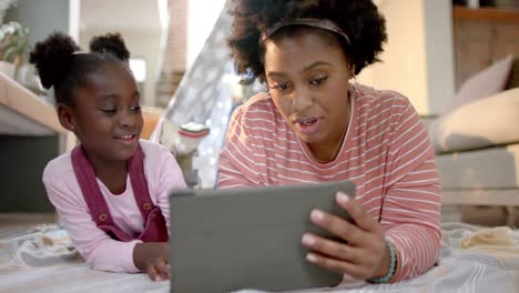 Happy-african-american-mother-and-daughter-lying-outside-tent-and-using-tablet-at-home,-slow-motion