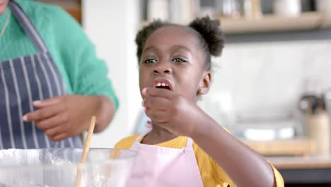 Happy-african-american-daughter-eating-blueberries-with-mother-in-kitchen,-slow-motion