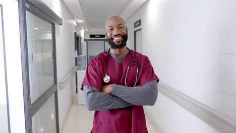 Porträt-Eines-Glücklichen-Afroamerikanischen-Männlichen-Arztes-Im-Krankenhausflur,-Zeitlupe