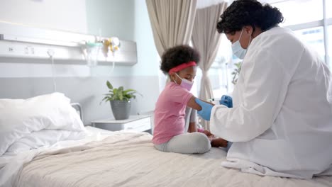 Afroamerikanische-Ärztin-Mit-Gesichtsmaske,-Die-Einem-Mädchen-Im-Krankenhauszimmer-Eine-Injektion-Verabreicht,-Zeitlupe