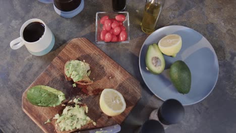 Close-up-of-avocado-sandwiches,-vegetables,-spices-and-coffee-in-kitchen,-slow-motion