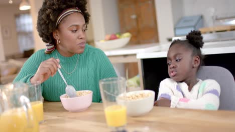 Madre-E-Hija-Afroamericanas-Comiendo-Cereales-Con-Leche-Y-Hablando-En-La-Cocina,-Cámara-Lenta