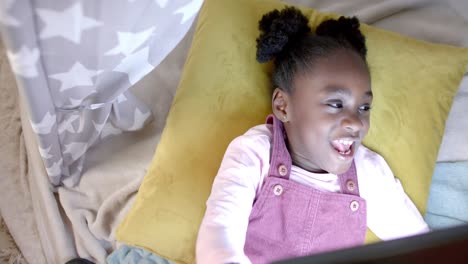 Happy-african-american-girl-lying-in-tent-and-using-tablet-at-home,-slow-motion