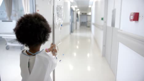 African-american-girl-with-drip-walking-in-hospital-corridor,-copy-space,-slow-motion