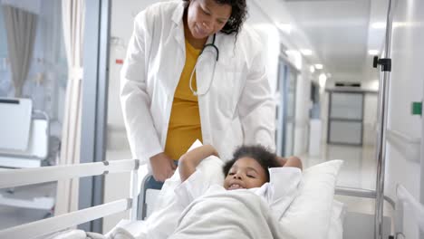 African-american-female-doctor-staying-over-girl-lying-in-hospital-bed-in-corridor,-slow-motion