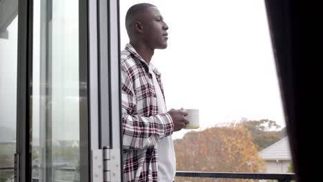 African-american-man-standing-on-balcony-and-drinking-coffee-at-home,-slow-motion