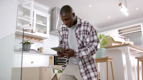 Afroamerikanischer-Mann-Sitzt-Auf-Der-Treppe-In-Der-Küche-Und-Benutzt-Zu-Hause-Ein-Tablet,-Zeitlupe