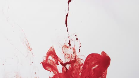Slow-motion-video-of-red-watercolor-ink-mixing-in-water-against-grey-background