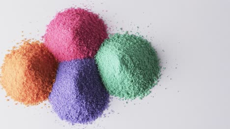 Video-of-close-up-of-heaps-of-multi-coloured-sand-grains-and-copy-space-on-white-background