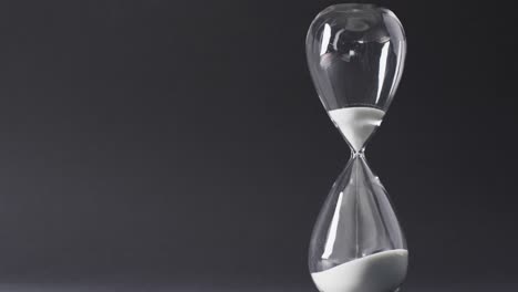 Video-of-hourglass-with-sand-pouring,-copy-space-on-black-background